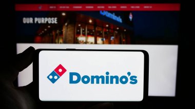 Stuttgart, Almanya - 12-09-2023: ABD 'li restoran zinciri Domino' s Pizza Inc. 'in logosuyla cep telefonu sahibi kişi iş sayfasının önünde. Telefon ekranına odaklan.