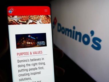 Stuttgart, Almanya - 12-09-2023: Logo önünde ABD 'li restoran zinciri şirketi Domino' s Pizza Inc. 'in web sayfası ile akıllı telefon tutan kişi. Telefon ekranının merkezine odaklan.