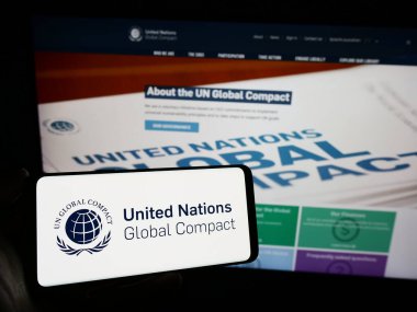 Stuttgart, Almanya - 12-09-2023: Web sayfası önünde BM Paktı Global Compact logosu olan cep telefonu sahibi kişi. Telefon ekranına odaklan.