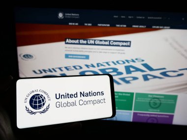 Stuttgart, Germany - 12-09-2023: Person holding mobile phone with logo of UN pact United Nations Global Compact in front of web page. Focus on phone display. clipart