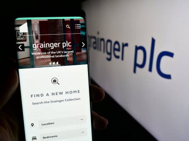 Stuttgart, Almanya - 12-12-2023: İngiliz yerleşim şirketi Grainger plc 'in logolu web sayfası ile akıllı telefon tutan kişi. Telefon ekranının merkezine odaklan.