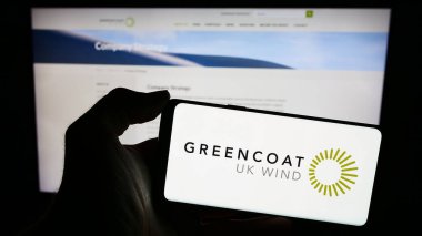 Stuttgart, Almanya - 12-12-2023: İngiliz yatırım şirketi Greencoat UK Wind plc 'in logosuna sahip cep telefonu sahibi kişi iş sayfasının önünde. Telefon ekranına odaklan.