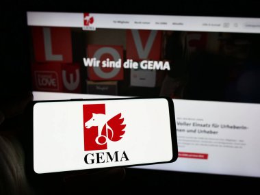 Stuttgart, Almanya - 12-14-2023: İnternet sitesi önünde üzerinde Alman toplama toplumu GEMA logosu olan akıllı telefon taşıyan kişi. Telefon ekranına odaklan.