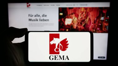 Stuttgart, Almanya - 12-14-2023: İnternet sayfası önünde Alman toplama toplumu GEMA logosu olan cep telefonu sahibi kişi. Telefon ekranına odaklan.