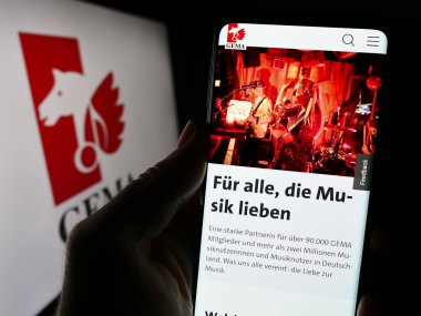 Stuttgart, Almanya - 12-14-2023: Alman toplama toplumu GEMA 'nın web sayfası ile logo önünde akıllı telefon tutan kişi. Telefon ekranının merkezine odaklan.