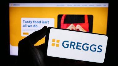 Stuttgart, Almanya - 12-14-2023: İngiliz fırın zinciri Greggs plc 'in logosuna sahip akıllı telefon sahibi kişi web sitesinin önünde. Telefon ekranına odaklan.