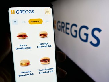 Stuttgart, Almanya - 12-14-2023: İngiliz fırın zinciri Greggs plc 'in web sayfası ile akıllı telefon sahibi kişi iş logosu önünde. Telefon ekranının merkezine odaklan.