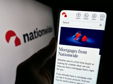 Stuttgart, Germany - 12-14-2023: Person holding cellphone with webpage of British financial institution Nationwide Building Society with logo. Focus on center of phone display. clipart