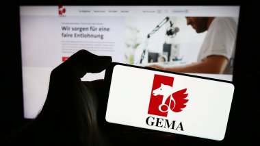 Stuttgart, Almanya - 12-14-2023: İnternet sayfası önünde Alman toplama derneği GEMA logosu taşıyan kişi. Telefon ekranına odaklan.