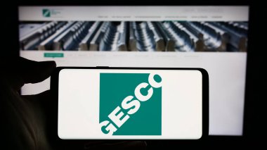 Stuttgart, Almanya - 12-14-2023: Alman işlem mühendisliği şirketi GESCO SE 'nin logosuyla cep telefonu sahibi kişi iş sayfasının önünde. Telefon ekranına odaklan.