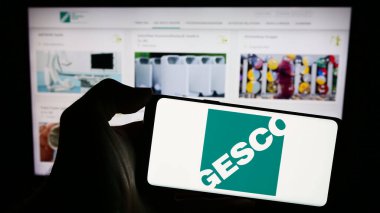 Stuttgart, Almanya - 12-14-2023: Üzerinde Alman işlem mühendisliği şirketi GESCO SE 'nin logosu bulunan cep telefonu sahibi kişi iş sayfasının önünde. Telefon ekranına odaklan.
