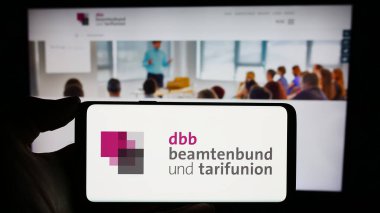 Stuttgart, Almanya - 12-14-2023: İnternet sayfası önünde sendika merkezi DBB Beamtenbund und Tarifunion logosu olan kişi. Telefon ekranına odaklan.