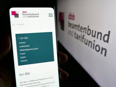 Stuttgart, Almanya - 12-14-2023: Sendika merkezi DBB Beamtenbund und Tarifunion 'ın web sitesi ile logo önünde akıllı telefon tutan kişi. Telefon ekranının merkezine odaklan.