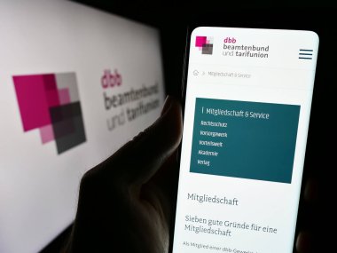 Stuttgart, Almanya - 12-14-2023: Sendika merkezi DBB Beamtenbund und Tarifunion 'ın internet sayfası logo önünde cep telefonu tutan kişi. Telefon ekranının merkezine odaklan.