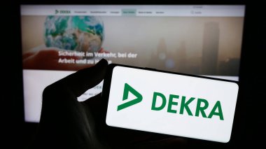 Stuttgart, Almanya - 12-14-2023: Alman uzman örgütü DEKRA 'nın logosunun bulunduğu akıllı telefonu web sitesi önünde tutan kişi. Telefon ekranına odaklan.