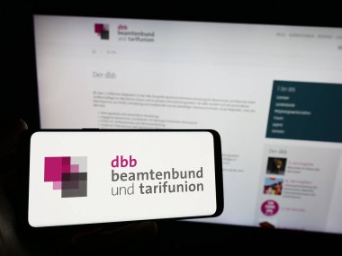 Stuttgart, Almanya - 12-14-2023: İnternet sitesi önünde sendika merkezi DBB Beamtenbund und Tarifunion logosuna sahip kişi. Telefon ekranına odaklan.