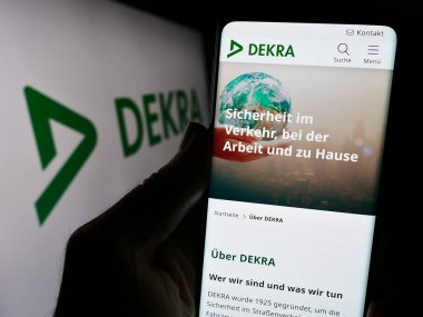 Stuttgart, Almanya - 12-14-2023: İş logosu önünde Alman uzman örgütü DEKRA 'nın web sayfası ile cep telefonu tutan kişi. Telefon ekranının merkezine odaklan.
