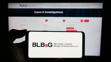 Stuttgart, Germany - 12-15-2023: Person holding smartphone with logo of US law firm Bernstein Litowitz Berger and Grossmann (BLBG) in front of website. Focus on phone display. clipart