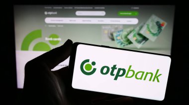 Stuttgart, Almanya - 12-15-2023: Macar finans hizmetleri şirketi OTP Bank Group 'un logosunun bulunduğu akıllı telefon sahibi kişi web sitesi önünde. Telefon ekranına odaklan.