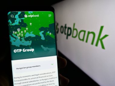 Stuttgart, Germany - 12-15-2023: Person holding smartphone with web page of Hungarian financial services company OTP Bank Group in front of logo. Focus on center of phone display. clipart