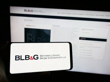 Stuttgart, Almanya - 12-15-2023: İnternet sayfası önünde ABD 'li hukuk firması Bernstein Litowitz Berger ve Grossmann' ın (BLBG) logosuyla cep telefonu tutan kişi. Telefon ekranına odaklan.