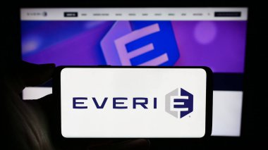 Stuttgart, Almanya - 12-17-2023: ABD 'li slot makinesi şirketi Everi Holding Inc.' in logosuyla cep telefonu sahibi kişi iş sayfasının önünde. Telefon ekranına odaklan.