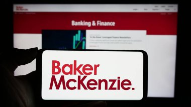 Stuttgart, Almanya - 12-17-2023: ABD 'li hukuk firması Baker McKenzie' nin logosuyla cep telefonu sahibi kişi iş sayfasının önünde. Telefon ekranına odaklan.