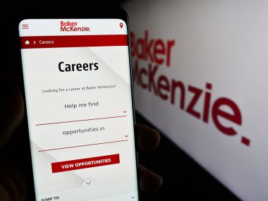 Stuttgart, Almanya - 12-17-2023: ABD 'li hukuk firması Baker McKenzie' nin web sayfası ile şirket logosu önünde cep telefonu tutan kişi. Telefon ekranının merkezine odaklan.