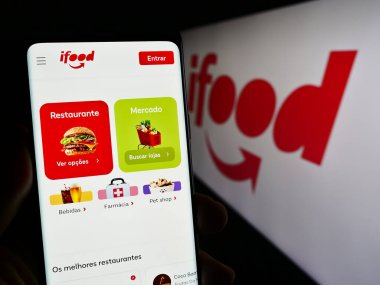 Stuttgart, Almanya - 12-18-2023: Cep telefonunda Brezilya gıda siparişi ve teslimat şirketi iFood 'un web sayfası bulunan kişi logonun önünde. Telefon ekranının merkezine odaklan.