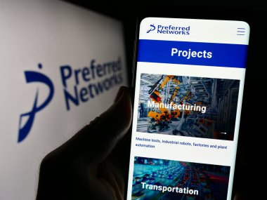 Stuttgart, Almanya - 12-18-2023: Yapay zeka şirketi Preferred Networks Inc. 'in logolu web sayfası ile cep telefonu tutan kişi. Telefon ekranının merkezine odaklan.
