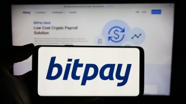 Stuttgart, Almanya - 12-18-2023: Üzerinde ABD kripto para ödeme şirketi BitPay Inc. 'in logosu bulunan cep telefonu sahibi kişi iş sayfasının önünde. Telefon ekranına odaklan.