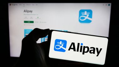 Stuttgart, Almanya - 12-19-2023: Çinli ödeme platformu şirketi Alipay 'in logosuna sahip cep telefonu sahibi kişi iş sayfasının önünde. Telefon ekranına odaklan.