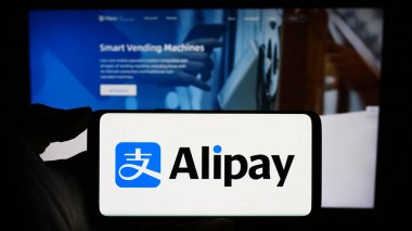 Stuttgart, Almanya - 12-19-2023: Çinli ödeme platformu şirketi Alipay 'in logosuyla cep telefonu tutan kişi iş sayfasının önünde. Telefon ekranına odaklan.