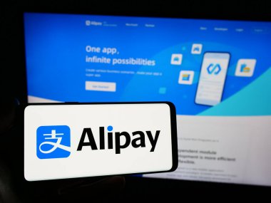 Stuttgart, Almanya - 12-19-2023: Çinli ödeme platformu şirketi Alipay 'in logosuna sahip akıllı telefon sahibi kişi web sitesinin önünde. Telefon ekranına odaklan.