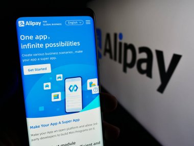 Stuttgart, Almanya - 12-19-2023: Çinli ödeme platformu şirketi Alipay 'in internet sayfası ile akıllı telefon taşıyan kişi iş logosu önünde. Telefon ekranının merkezine odaklan.
