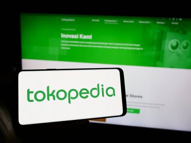 Stuttgart, Almanya - 12-20-2023: Endonezyalı e-ticaret şirketi PT Tokopedia 'nın logosunun bulunduğu cep telefonu sahibi kişi iş sayfasının önünde. Telefon ekranına odaklan.