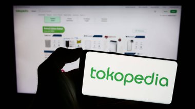 Stuttgart, Almanya - 12-20-2023: Endonezyalı e-ticaret şirketi PT Tokopedia 'nın logosunun bulunduğu cep telefonu sahibi kişi iş sayfasının önünde. Telefon ekranına odaklan.