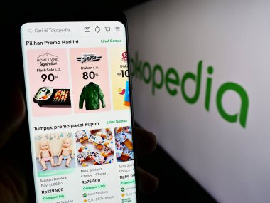 Stuttgart, Almanya - 12-20-2023: Endonezyalı e-ticaret şirketi PT Tokopedia 'nın logonun önündeki web sayfası ile akıllı telefon tutan kişi. Telefon ekranının merkezine odaklan.