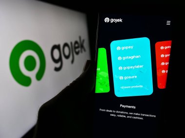 Stuttgart, Germany - 12-20-2023: Person holding cellphone with webpage of technology company PT Gojek Indonesia in front of business logo. Focus on center of phone display. clipart