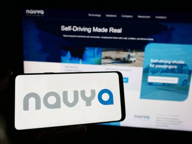 Stuttgart, Almanya - 12-20-2023: İnternet sitesinin önünde üzerinde Fransız otonom araç şirketi Navya S.A. 'nın logosu bulunan akıllı telefon sahibi kişi. Telefon ekranına odaklan.