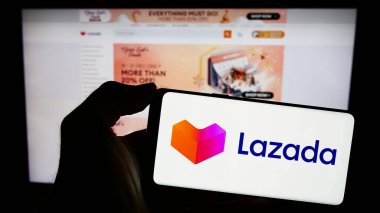 Stuttgart, Almanya - 12-20-2023: Asyalı e-ticaret şirketi Lazada Group 'un logosuna sahip cep telefonu sahibi kişi iş sayfasının önünde. Telefon ekranına odaklan.