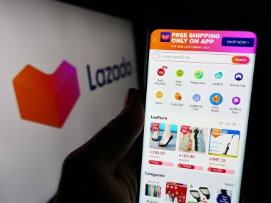 Stuttgart, Almanya - 12-20-2023: Asyalı e-ticaret şirketi Lazada Group 'un internet sayfası ile iş logosu önünde cep telefonu tutan kişi. Telefon ekranının merkezine odaklan.