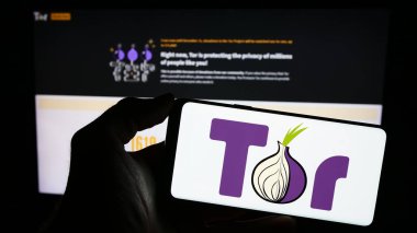 Stuttgart, Almanya - 12-20-2023: İnternet sayfasının önünde anonim iletişim yazılımı The Onion Router (TOR) logosu olan cep telefonu sahibi kişi. Telefon ekranına odaklan.