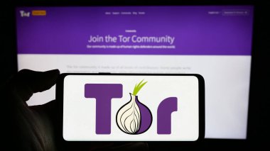 Stuttgart, Almanya - 12-20-2023: İnternet sayfasının önünde anonim iletişim yazılımı The Onion Router (TOR) logosu olan cep telefonu sahibi kişi. Telefon ekranına odaklan.