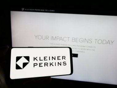 Stuttgart, Almanya - 12-20-2023: Amerikan risk sermayesi şirketi Kleiner Perkins 'in logosunun bulunduğu cep telefonu sahibi kişi iş sayfasının önünde. Telefon ekranına odaklan.
