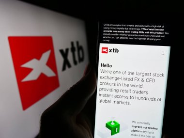 Stuttgart, Almanya - 12-22-2023: Polonyalı yatırım simsarı XTB S.A. 'nın web sitesi ile iş logosu önünde akıllı telefon tutan kişi. Telefon ekranının merkezine odaklan.