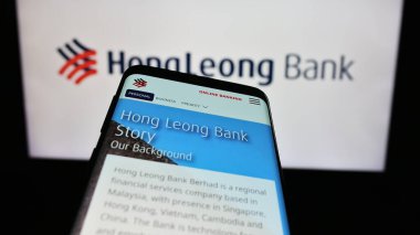 Stuttgart, Germany - 12-22-2023: Mobile phone with website of Malaysian financial company Hong Leong Bank Berhad in front of business logo. Focus on top-left of phone display. clipart