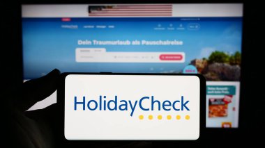 Stuttgart, Almanya - 11-02-2023: İsviçreli seyahat portalı şirketi Holidaycheck AG 'nin logosuna sahip akıllı telefon sahibi kişi web sitesi önünde. Telefon ekranına odaklan.