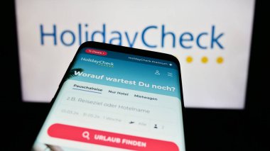 Stuttgart, Almanya - 11-02-2023: İş logosu önünde İsviçre seyahat rezervasyon portalı şirketi HolidayCheck AG 'nin web sitesi ile cep telefonu. Telefon ekranının sol üst kısmına odaklan.