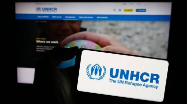 Stuttgart, Germany - 11-02-2023: Person holding mobile phone with logo of United Nations High Commissioner for Refugees (UNHCR) in front of web page. Focus on phone display. clipart